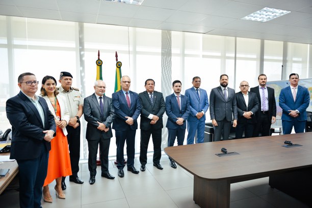 Na foto, doze pessoas, sendo dez homens e uma mulher, posam para a foto. À frente deles, uma mes...