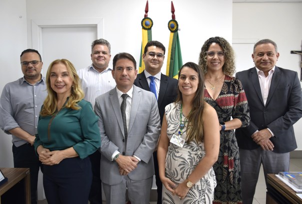 Na imagem, oito pessoas estão alinhadas em duas fileiras posando para foto, dentro da sala da Pr...