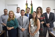 Na imagem, oito pessoas estão alinhadas em duas fileiras posando para foto, dentro da sala da Pr...