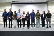 A imagem mostra dez pessoas alinhadas em pé, lado a lado, sobre o palco do auditório do TRE-CE. ...