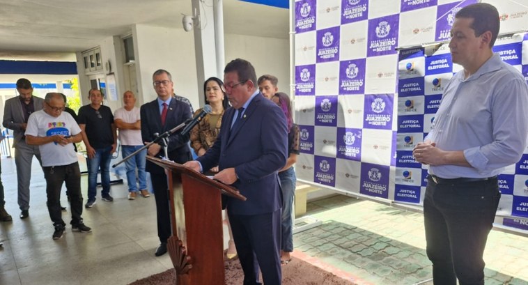 TRE-CE inaugura dois novos postos de atendimento em Juazeiro do Norte A imagem é um registro fotográfico horizontal. Nele, há um pátio, com paredes brancas, tapete ma...