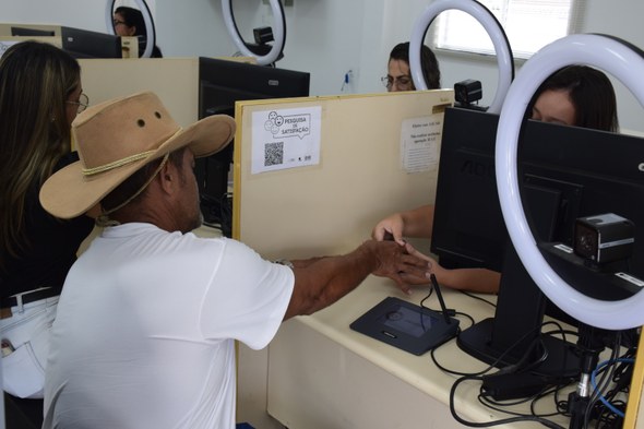 A foto mostra um atendimento eleitoral em andamento, no qual uma servidora da Justiça Eleitoral ...