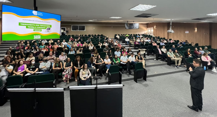 A imagem registra uma capacitação realizada no auditório do TRE-CE que possui piso cinza, parede...