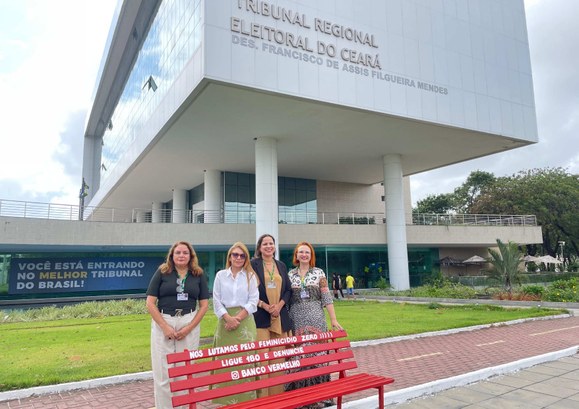 TRE-CE instala Banco Vermelho na sede, símbolo do combate à violência de gênero Na imagem, há quatro representantes da Ouvidoria posando na frente do prédio do Tribunal Regiona...