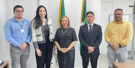 Na imagem, cinco pessoas estão em pé lado a lado, posicionadas em frente de duas bandeiras, uma ...