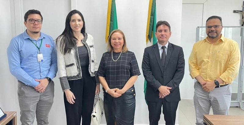 Na imagem, cinco pessoas estão em pé lado a lado, posicionadas em frente de duas bandeiras, uma ...