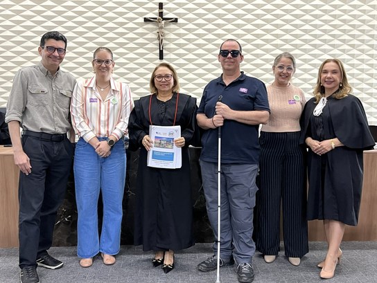 Na primeira foto, na sala de sessões, seis pessoas estão posicionadas lado a lado diante de uma ...