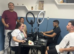 A imagem mostra dois atendimentos eleitorais sendo realizados em uma sala. No centro do ambiente...