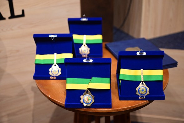 Registro fotográfico feito durante o evento. Nele, sobre uma mesa de madeira, estão quatro caixa...