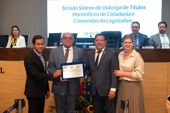 Registro fotográfico feito durante o evento. Nele, à frente de um banner com o título: "Sessão s...