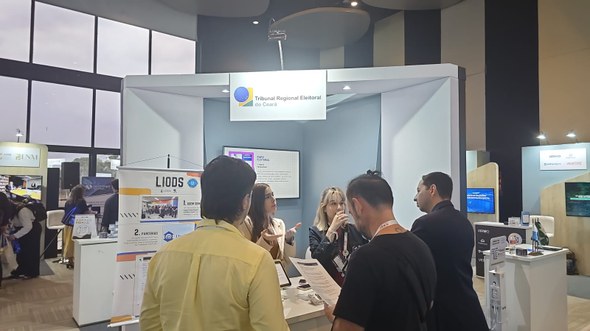 Registro fotográfico feito no ExpoJud. Nele, há o mesmo estande, com três estagiários do TRE-CE ...