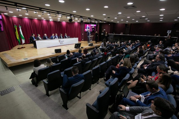 TRE-CE participa de encontro nacional dos dirigentes das escolas eleitorais O registro, no auditório, tem participantes sentados em cadeiras direcionada para o palco, onde ...