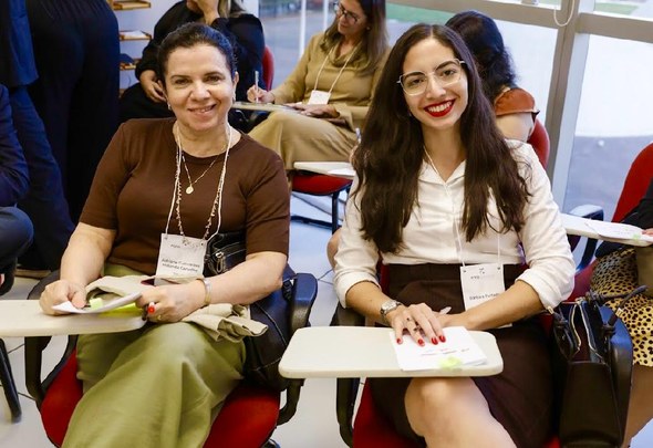 TRE-CE participa de oficina sobre diretrizes nacionais para ações de cidadania das escolas eleitorais, em Brasília Na imagem, aparecem as duas servidoras do TRE-CE sentadas lado a lado em cadeiras. Ambas usam cr...