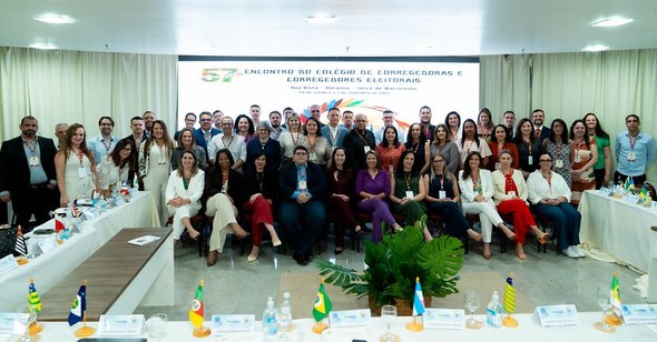 Na terceira imagem, um grupo numeroso de pessoas posa para foto em um auditório. Ao fundo, está ...