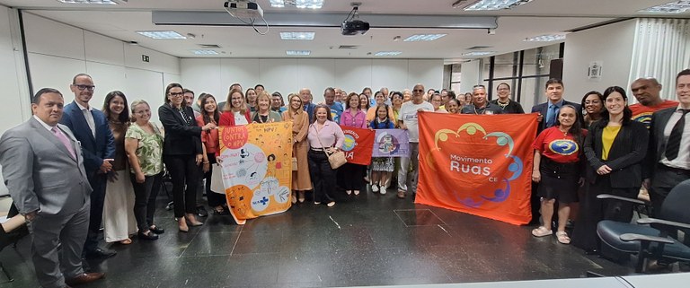 Na imagem, aproximadamente quarenta pessoas estão posicionadas em pé, organizadas em duas fileir...