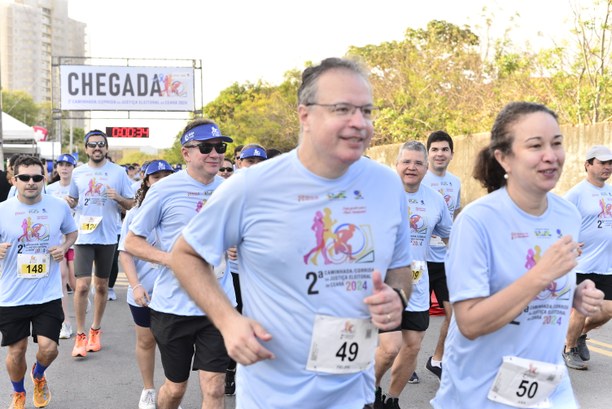 TRE-CE realiza 2ª Corrida/Caminhada da Justiça Eleitoral cearense No registro, há diversas pessoas em movimentação de corrida, usando blusa azul, com a logo e o t...