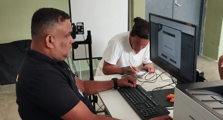 TRE-CE realiza ação de atendimento em presídio de Aquiraz A imagem é um registro fotográfico de um atendimento do TRE-CE. Em primeiro plano, está um servi...