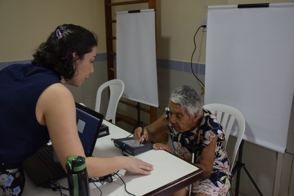 Na imagem, uma servidora do TRE-CE está sentada diante de um computador portátil e orienta uma m...