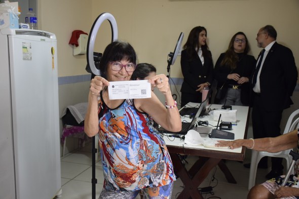 Uma mulher está em pé na frente de uma mesa de atendimento e segura um documento aberto com as d...