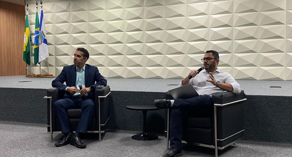 Registro fotográfico feito no auditório do TRE-CE. Nele, dois servidores estão sentados em poltr...