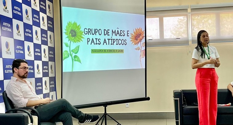 TRE-CE realiza primeiro encontro do grupo de Mães e Pais Atípicos A imagem retangular mostra uma sala de parede amarela. Há uma tela de projetor, com a apresentaç...