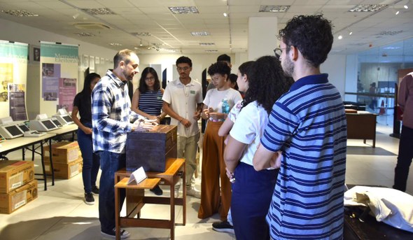 TRE-CE recebe 20 estudantes do curso de História da UVA em visita guiada Na e última imagem, Yuri Holanda Cruz aparece mostrando uma urna de madeira aos alunos.