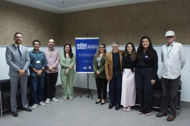 TRE-CE recebe, da UniCatólica, maquetes de sedes antigas para integrar acervo do Centro Memória Eleitoral Na imagem, um grupo de nove pessoas posicionadas lado a lado em um ambiente interno institucion...