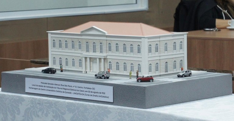 TRE-CE recebe, da UniCatólica, maquetes de sedes antigas para integrar acervo do Centro Memória Eleitoral Na imagem, a maquete aparece em destaque sobre a mesma mesa. A estrutura representa o edifício i...