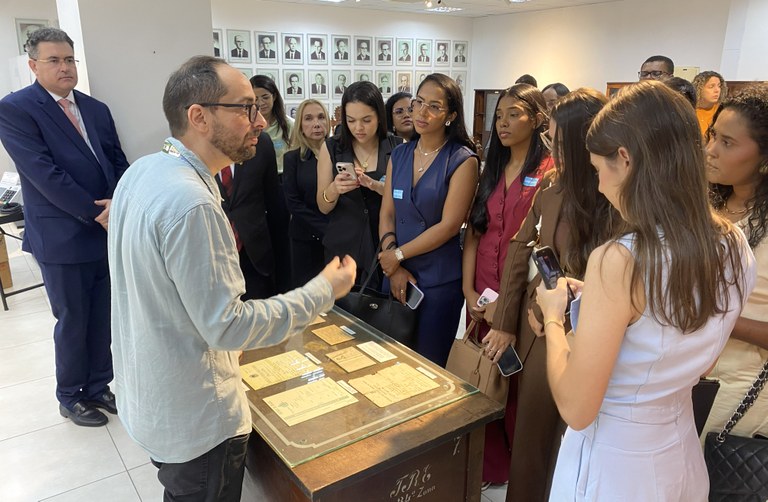 TRE-CE recebe grupo de advogados do Cariri e representantes da OAB-CE em visita institucional Na imagem, o grupo de advogados está reunido ao redor de uma mesa com objetos e documentos expos...