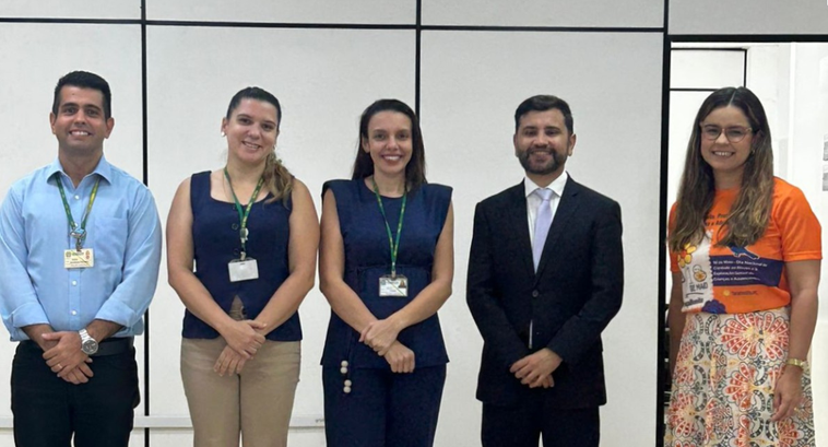 Na imagem, cinco pessoas estão em pé lado a lado em um ambiente interno da 7ª Zona Eleitoral. No...