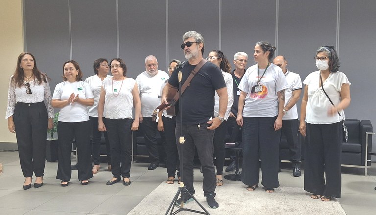 Na imagem mostra o grupo coral Vozes de Justiça, composto por homens e mulheres. Eles vestem cal...