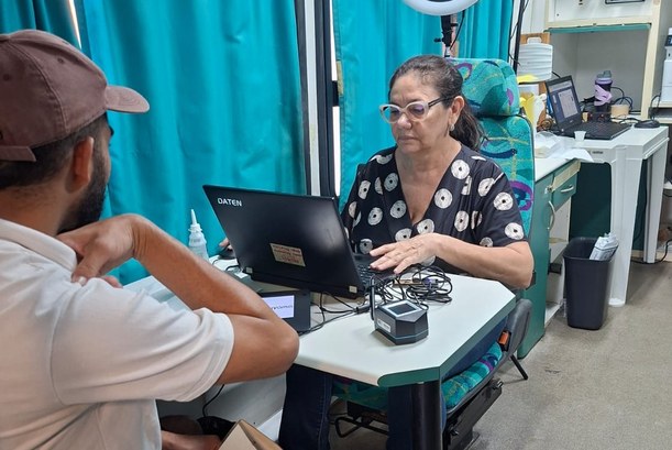A imagem mostra um atendimento eleitoral em andamento dentro do ônibus do TRE-CE. Um eleitor est...