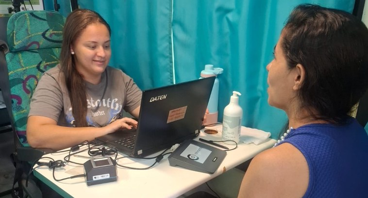 A imagem mostra duas mulheres sentadas frente a frente em uma mesa: uma servidora do TRE-CE e um...