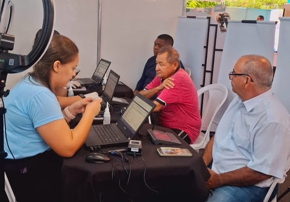 Unidade Móvel do TRE-CE realiza 98 atendimentos no Genibaú, em Fortaleza A imagem mostra atendimentos eleitorais sendo realizados. Em primeiro plano, há uma mesa coberta...