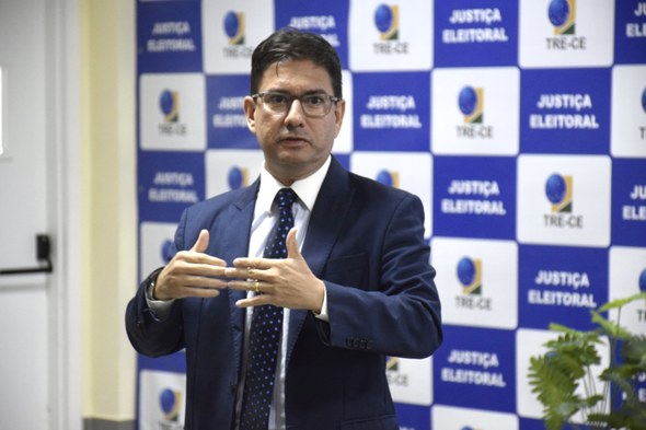 Visita ao TRE-CE aproxima estudantes de Direito da UVA da prática do processo eleitoral Na imagem, o juiz está ao centro, discursando para os estudantes. Ao fundo, há um banner que cob...